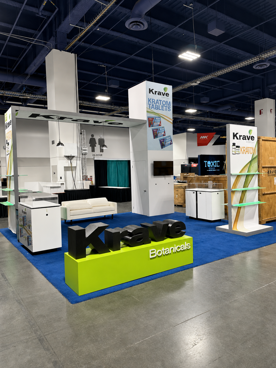 Krave Botanicals trade show booth with white display towers, seating and blue carpet